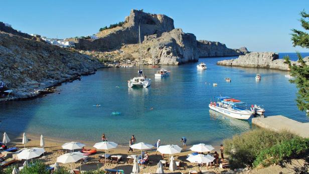 Blick auf eine malerische Bucht mit Strand, Booten und einem Felsen im Hintergrund.