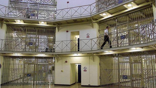Ein Gefängnisinnenraum mit mehreren Ebenen von Zellen und einem Wachmann, der auf einem Steg geht.