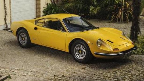 Ein gelber Ferrari Dino 246 GT steht auf einem gepflasterten Weg.