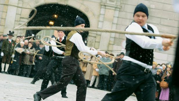 Männer in Tracht nehmen an einem Brauchtum mit Seilen im Schnee teil.