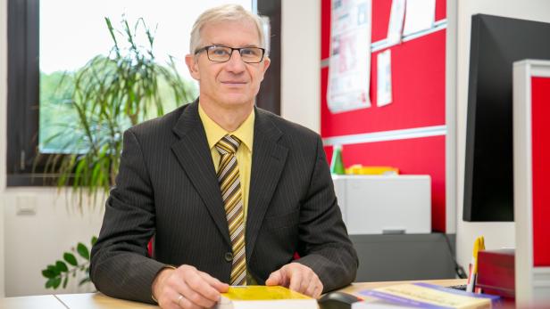 Ein Mann mit Brille und Anzug sitzt an einem Schreibtisch mit Büchern.
