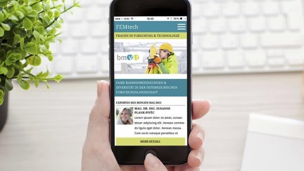 Eine Hand hält ein Smartphone, das die FEMtech-Webseite anzeigt.