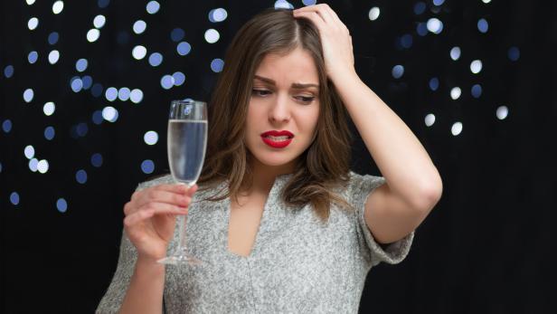 Eine Frau mit rotem Lippenstift blickt besorgt auf ein Glas Sekt.