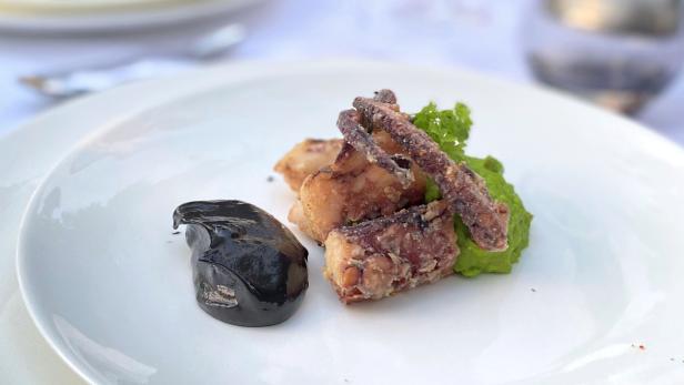 Ein Teller mit frittiertem Fisch, Tintenfischtinte und grünem Püree wird serviert.
