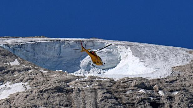 Ein gelber Hubschrauber fliegt vor einem Gletscher in den italienischen Bergen.