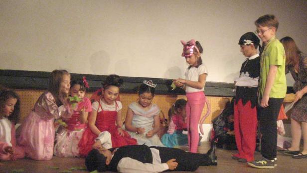 Kinder in Kostümen spielen ein Theaterstück, bei dem ein Junge am Boden liegt.