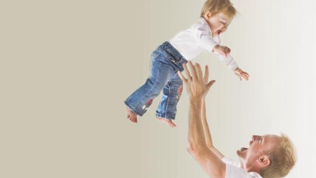 Ein Vater wirft sein lachendes Kind in die Luft.