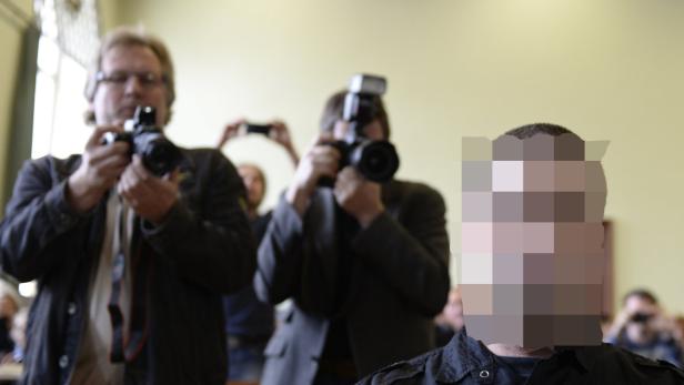 Fotografen umringen eine Person, deren Gesicht unkenntlich gemacht wurde.