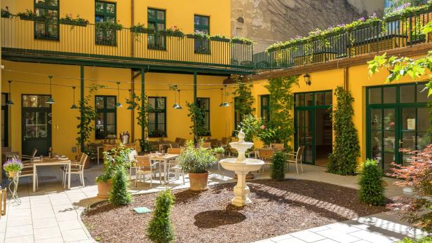 Ein Innenhof mit gelben Wänden, einem Brunnen und Tischen für ein Restaurant.