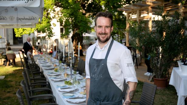 Ein Koch steht vor einer langen, festlich gedeckten Tafel im Freien.