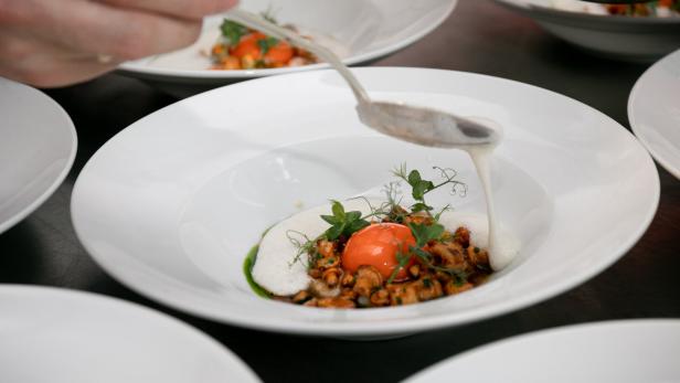Ein Koch garniert ein Gericht mit Pilzen und einem pochierten Eigelb mit einer Soße.