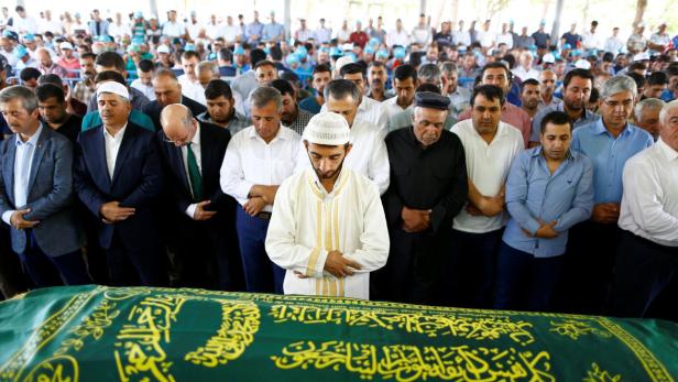 Eine Gruppe von Männern betet vor einem mit Kalligraphie bedeckten Sarg.