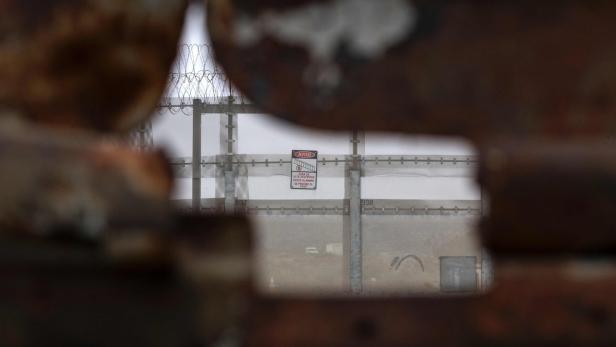 Ein Zaun mit Stacheldraht und einem Warnschild, gesehen durch eine Öffnung.