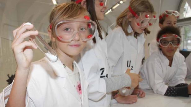 Eine Gruppe Kinder in Laborkitteln und Schutzbrillen experimentiert mit Chemikalien.