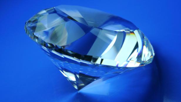 Ein geschliffener Diamant liegt auf einem blauen Untergrund.