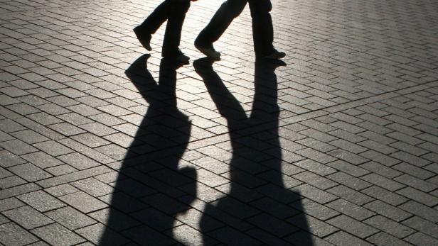 Die Schatten von zwei Personen, die auf einem gepflasterten Weg gehen.