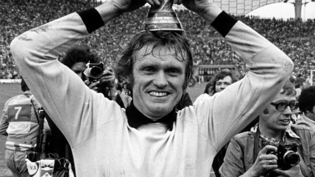 Franz Beckenbauer hält den Weltpokal auf seinem Kopf, umgeben von jubelnden Fans.