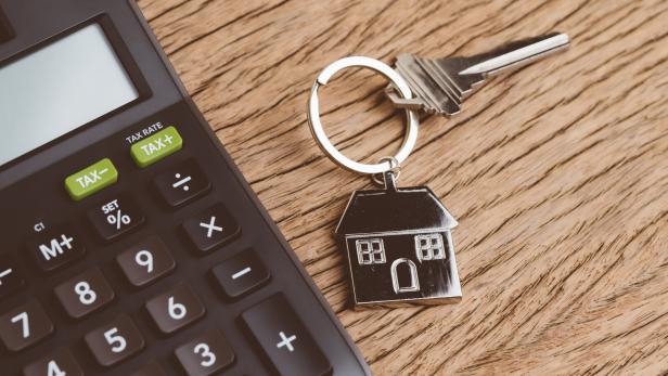 Mortgage calculation or buy and sell house, property and real estate, home key with house keyring or keychain with black calculator on wooden table