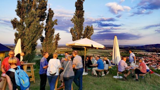 Menschen sitzen und stehen bei Sonnenuntergang im Freien zusammen.