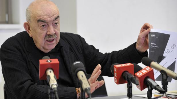 Ein Mann mit Schnurrbart präsentiert einen Bericht von KPMG mit dem Titel „Projekt Sopran“ vor Mikrofonen.