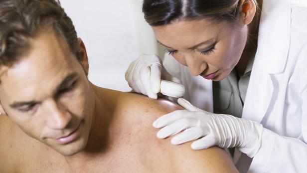Eine Hautärztin untersucht die Haut eines Mannes mit einem Vergrößerungsglas.