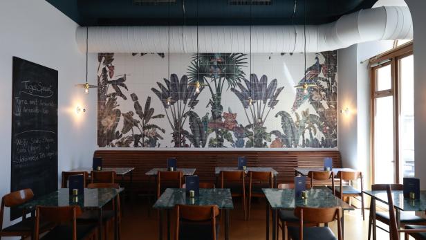 Ein Restaurant mit Tischen und Stühlen vor einer Wand mit Dschungelmotiven.