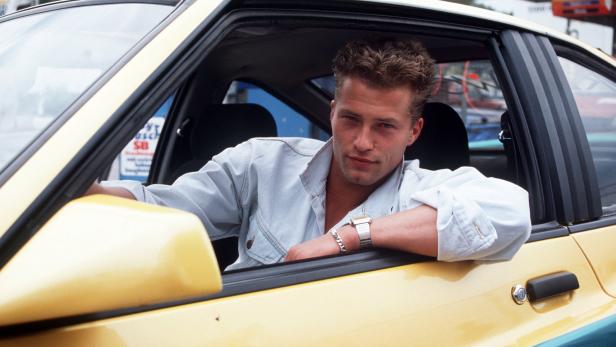 Ein Mann lehnt aus dem Fenster eines gelb-türkisfarbenen Autos.