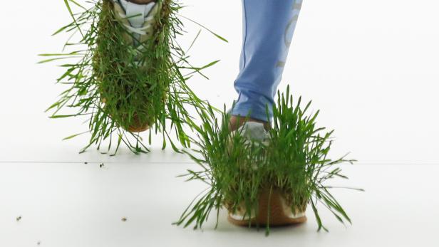 Ein Model präsentiert Schuhe, die mit Gras bewachsen sind, auf dem Laufsteg von Loewe.