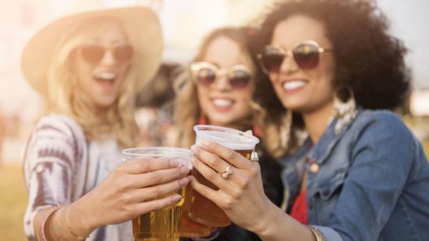 Drei junge Frauen stoßen mit Bier auf einem Festival an.