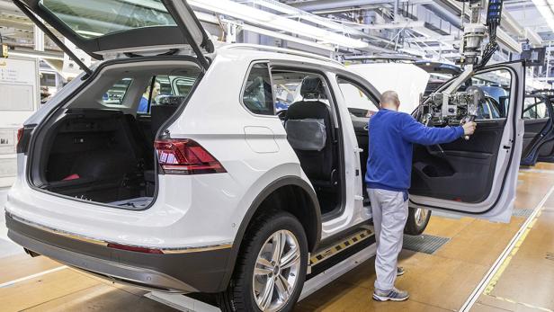 Ein Arbeiter montiert eine Tür an einem weißen Auto in einer Fabrikhalle.