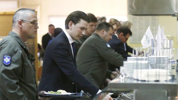 Menschen stehen an einem Buffet und nehmen Essen auf Teller.