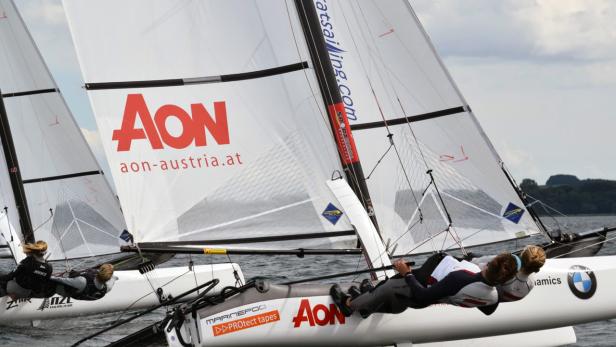 Zwei Segler auf einem Katamaran mit dem AON-Logo segeln auf dem Wasser.