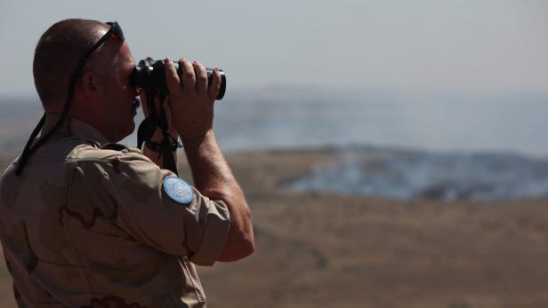 epa03734817 A UN peacekeeper watches with binoculars the Quneitra crossing (pictured in the backround), the only crossing between the Israel and Syria, in the Golan Heights, 07 June 2013. Clashes erupted on 07 June between Syrian government troops and rebels at a border crossing near the Israeli-occupied Golan Heights, activists said, a day after Damascus said it had regained control of the outpost. The pro-opposition Syrian Observatory for Human Rights, a Britain-based group monitoring the situation inside Syria, said fighting was raging in the town of Quneitra on the Syrian side of the Golan Heights. EPA/ATEF SAFADI