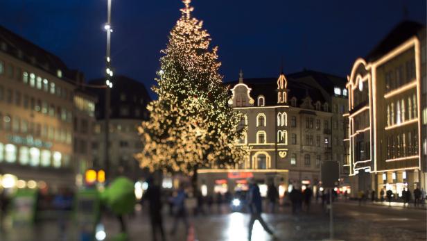 Ein großer, beleuchteter Weihnachtsbaum auf einem Platz in der Stadt bei Nacht.