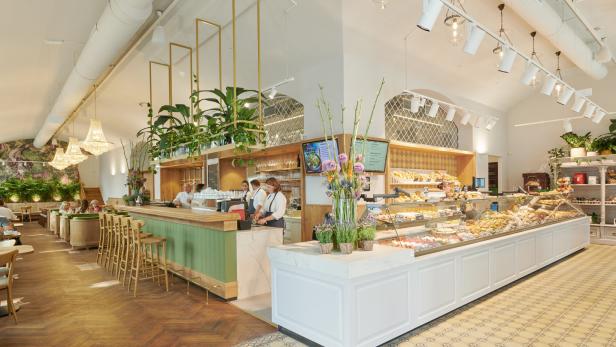 Innenansicht eines hellen Cafés mit Theke, Auslagen und Sitzbereich.