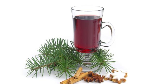 Ein Glas Glühwein mit Zimtstangen, Sternanis, Tannenzweig und Zimtsternen dekoriert.