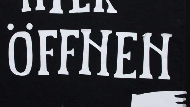 Ein Schild mit der Aufschrift „Bitte hier öffnen“ und zwei Händen.