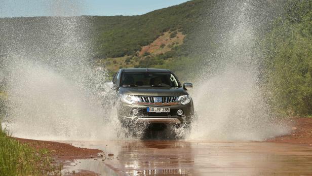 Ein grauer Mitsubishi L200 fährt durch eine Wasserpfütze.