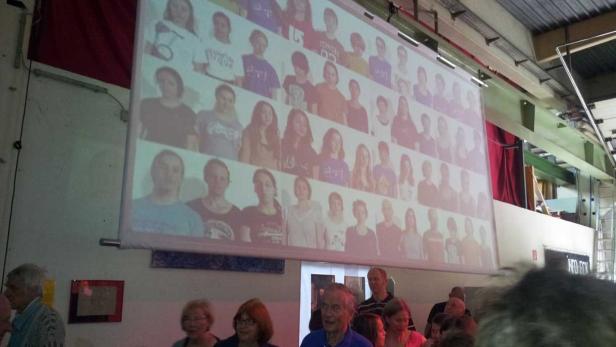 Eine Gruppe von Menschen schaut auf eine Leinwand mit vielen Porträts.