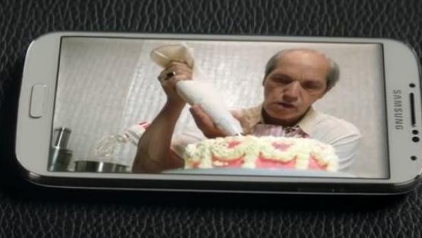 Ein Mann verziert auf dem Bildschirm eines Samsung-Smartphones eine Torte mit rosa Zuckerguss.