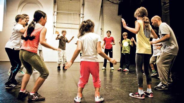 Eine Gruppe Kinder und ein Erwachsener tanzen oder spielen in einem Raum.