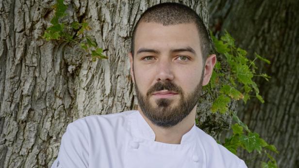 Ein Mann in Kochuniform lehnt an einem Baum.