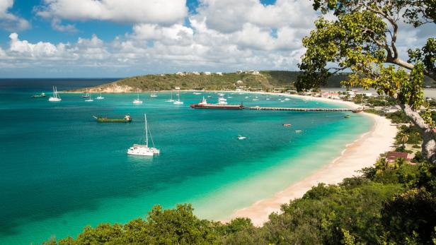 Blick auf eine tropische Bucht mit türkisfarbenem Wasser, einem Sandstrand und mehreren Booten.