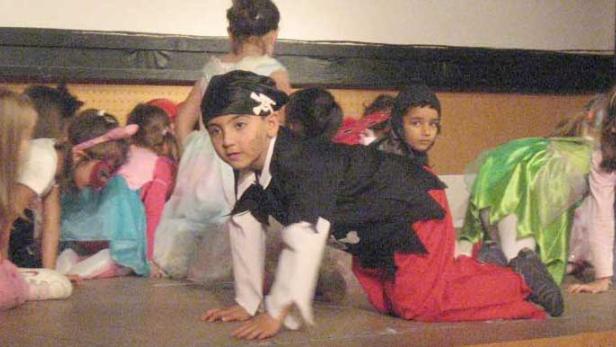 Eine Gruppe von Kindern in Kostümen sitzt auf einer Bühne.