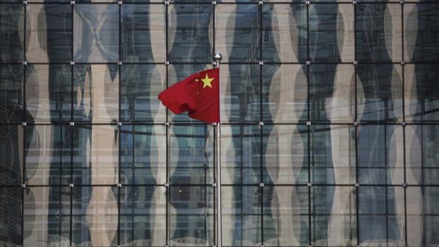 Die chinesische Nationalflagge weht vor einem modernen Glasgebäude.