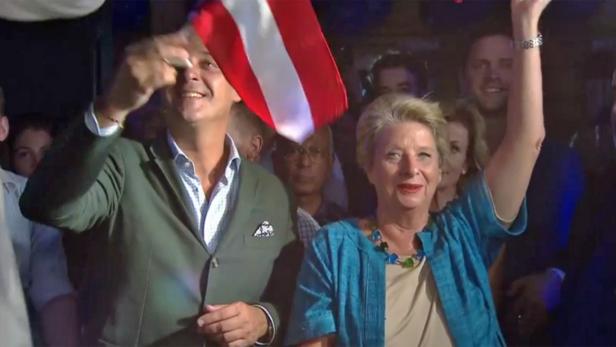 Ein Mann schwenkt eine österreichische Flagge, während eine Frau daneben jubelt.