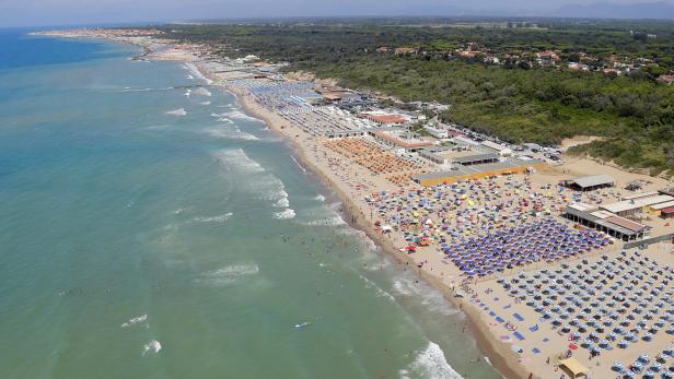 Luftaufnahme eines belebten Strandes mit vielen Sonnenschirmen und Badegästen.