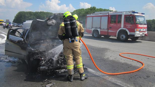 Feuerwehrleute löschen ein ausgebranntes Auto auf einer Autobahn.