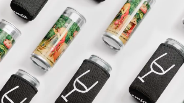 Mehrere Dosen Djuces, einige mit Getränkehaltern mit Weinglas-Logo, liegen auf einer weißen Oberfläche.