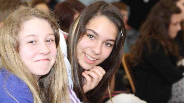 Zwei lächelnde junge Frauen sitzen nebeneinander in einem Raum.